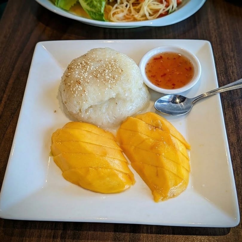 Sri Thai's mango sticky rice dessert with two mango slices, sticky rice, and sweet sauce.