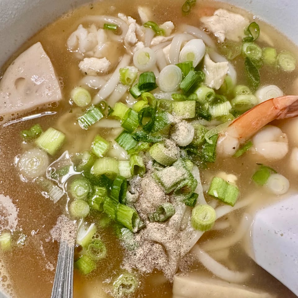 Close-up of a bowl of Vietnamese hu tieu with noodles, shrimp, pork, and green onions.