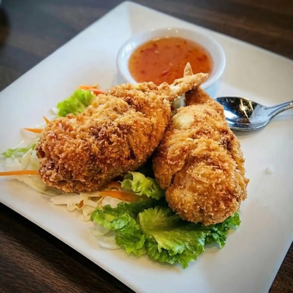 Two golden-brown fried shrimp on a bed of lettuce with a side of sweet chili sauce.