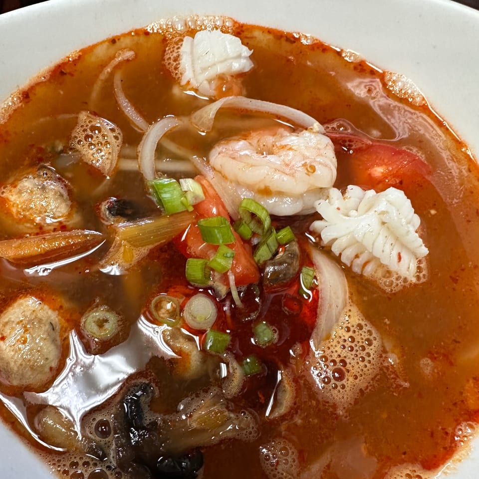 Close-up of a spicy seafood noodle soup with shrimp, squid, and green onions.