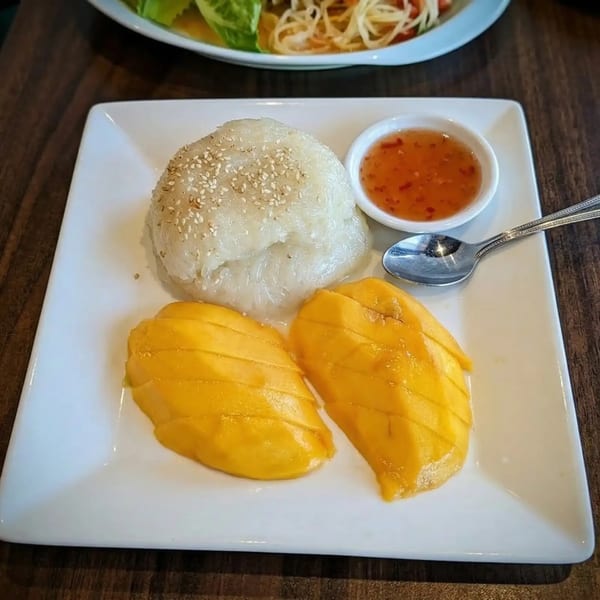 Mango sticky rice with sesame seeds and a sweet chili dipping sauce on a white plate.
